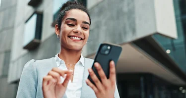 Lächelnde Geschäftsfrau, die ein Smartphone in der Hand hält.