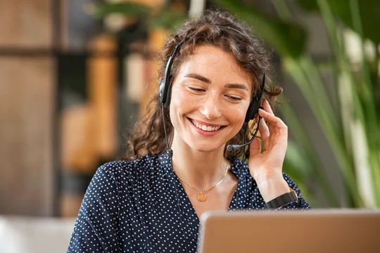 Junge Frau sitzt lächelnd am Schreibtisch, arbeitet am Laptop und telefoniert gleichzeitig mit einem Kunden – typische Szene einer Service-Desk-Beraterin im Callcenter.