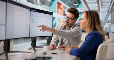 Zwei IT-Fachkräfte prüfen Cybersecurity-Warnmeldungen an mehreren Monitoren.
