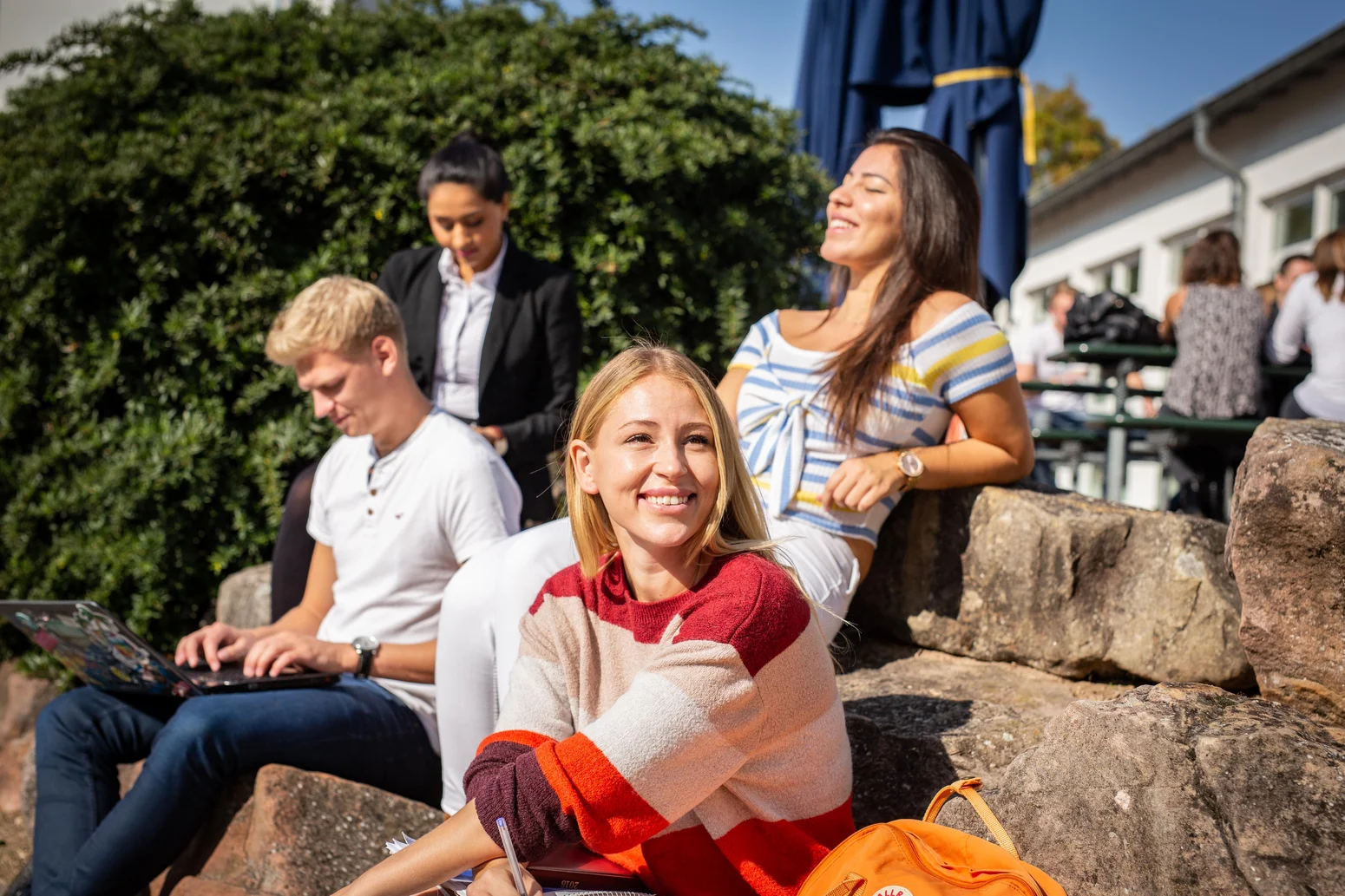 Eine Gruppe Studierender genießt die Pause in der Sonne vor der Mensa der Hochschule Worms.