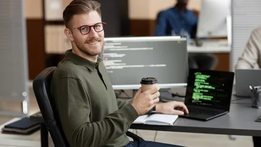 IT-Abteilungsleiter an einem Arbeitsplatz mit mehreren Bildschirmen und Programmcode.