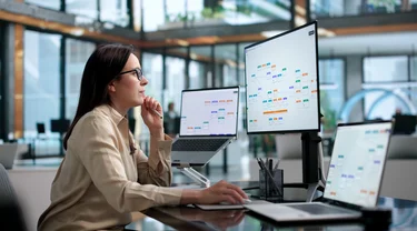 Frau analysiert digitale Workflow- und Prozessdarstellungen an mehreren Bildschirmen.