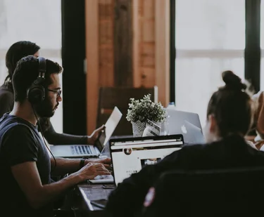 Informatik-Studierende arbeiten gemeinsam mit Laptops an einem großen Tisch.
