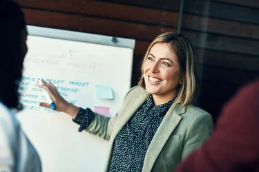 Eine Projektmanagerin vor einem Whiteboard stellt Strategien und Ideen vor.
