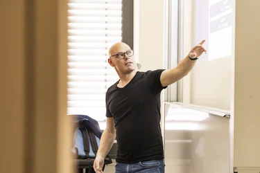 Ein Professor steht vor einer Leinwand und zeigt auf etwas in seiner Präsentation.