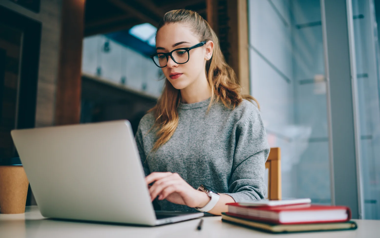 Interessierte Studentin informiert sich online über Studiengänge und Angebote der Hochschule. Über WLAN mit dem Internet verbunden, recherchiert die aufgeschlossene junge Frau mit Laptop und Brille gezielt nach passenden Studienmöglichkeiten.