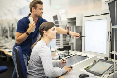 Ein Lotse und eine Lotsin blicken in einem Control Center der Flugsicherung auf die Bildschirme.