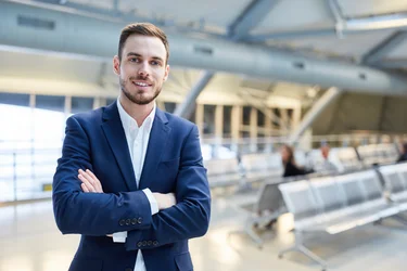 Selbstbewusster junger Geschäftsmann mit verschränkten Armen im Flughafenterminal