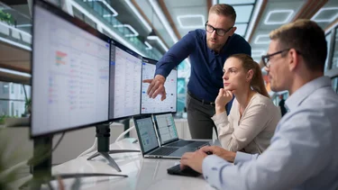 Berater erklärt einem Team digitale Unternehmenslösungen an mehreren Bildschirmen.