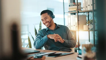 Mann mit Headset sitzt vor PC und lächelt